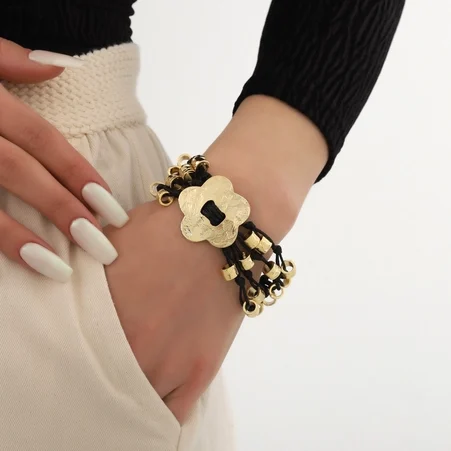 Bracelet Femme en Cuir Plaqué Or Bracelet noir et doré avec une fleur et des perles, porté sur un poignet.